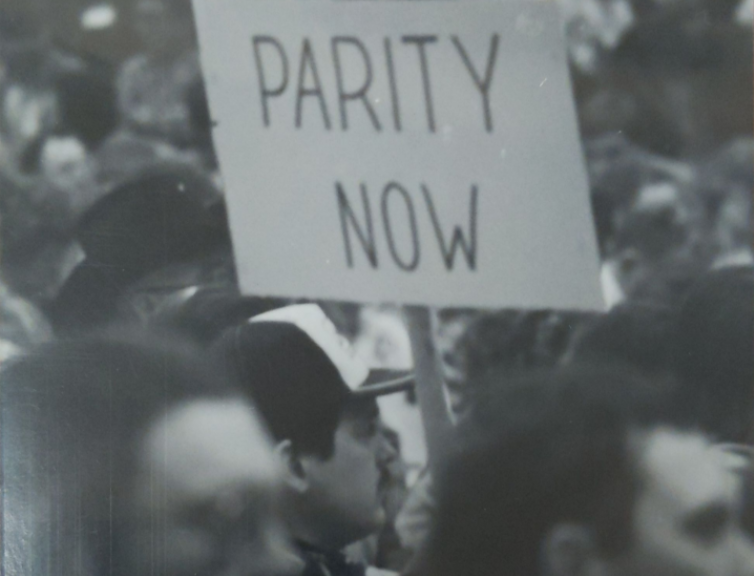 A man holds a sign reading "Parity Now" at the 1985 Pierre Farm Crisis Rally.